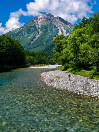 A man walking along the shore of a mountain riverの写真素材