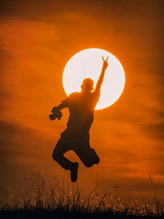Silhouette of a young man jumping in front of the sunの写真素材