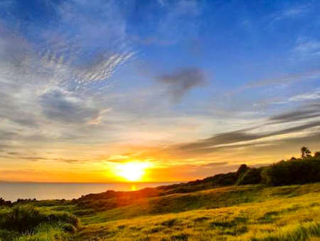 Sunset over the ocean with clouds in the sky and a grassy fieldの写真素材