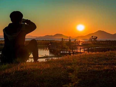 Silhouette of a man taking a photo of sunset at the lakeの写真素材