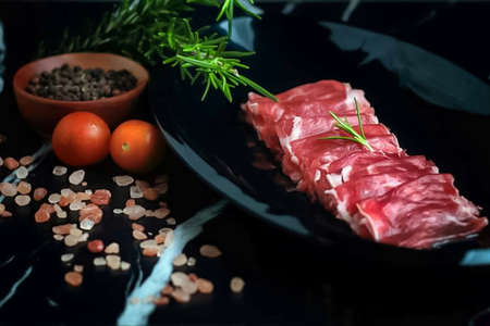 Raw beef steak on black plate with rosemary, salt and tomatoesの写真素材