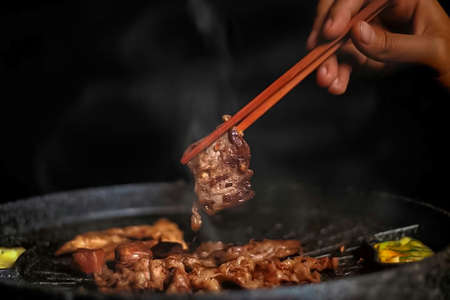 Close up of a man's hand holding a chopstick and cooking a yakiniku wokの写真素材