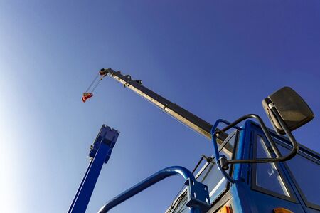 Cabin and hydraulic boom of crane with hook against blue sky. View from below.