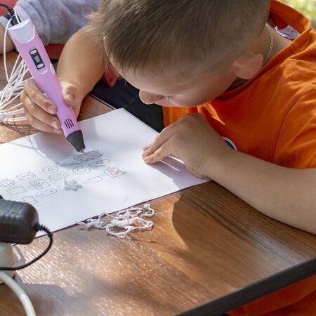 Child draws 3D pen on piece of paper. Top side view. Close up. Surgut, Russia - September 25, 2019.