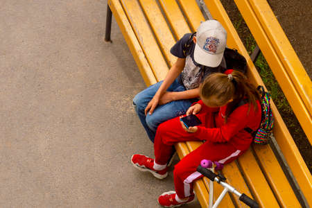 Children sit on bench with smartphone. Boy and girl. View from above. Surgut, Russia - 20 March 2020のeditorial素材