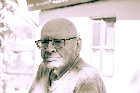 Old bald grandfather with glasses. Under the bright summer sun. Portrait.