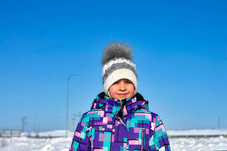 The girl squints from the bright winter sun. Sunny winter day. Front view.の写真素材