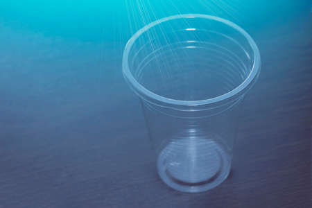 Transparent plastic cup on the table. View from the front from above. Rays of blue color.