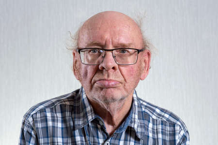 Old unshaven bald man with glasses. Indoors in daylight. Front view.の写真素材