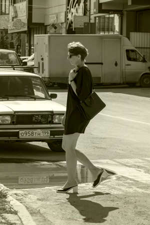 Woman with bag crosses the road. Sepia. Sunny autumn day. Side view. Crimea, Sudak - 10 October 2020.のeditorial素材