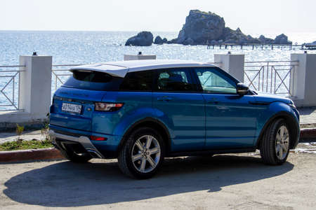 Car is blue Range Rover Evoque on black sea embankment. Sunny autumn day. Side view. Crimea, Sudak - 10 October 2020.のeditorial素材