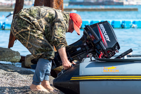 A man lifts the boat's engine. Sunny autumn day. Side view. Crimea, Sudak - 10 October 2020.