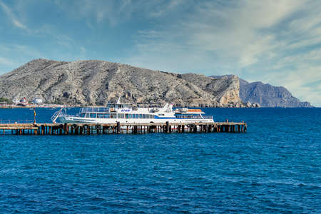 Black sea and boat, pier. View of Mount Alchak. Crimea, Sudak - 10 October 2020.のeditorial素材
