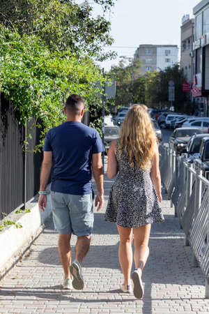 Man and woman pair walk along pavement road. Crimea, Sudak - 10 October 2020.