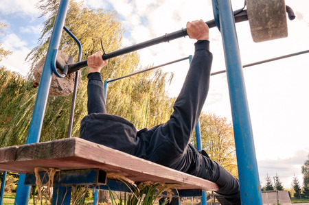 The athlete presses the bar in the nature .