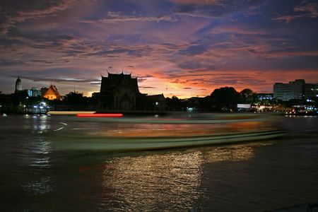 A boat leaves streaking lights on the Chao Praya River in Bangkok, shortly after a storm at sunset produces a dramatic skyの写真素材
