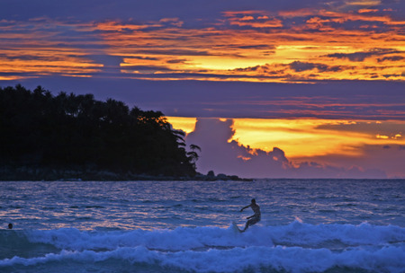 A colorful sky after a dramatic sunset in Phuket, Thailand. Surfer riding a wave in the foreground
