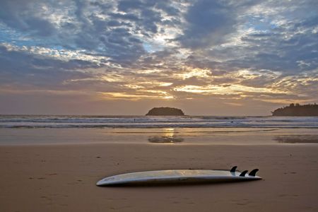 Sunset on a tropical beach with a surfboard in the foreground