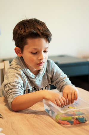 Poznan, Poland - May 15, 2020: Six years old young Caucasian Polish boy playing with plastic toy fish in a container by a table.のeditorial素材
