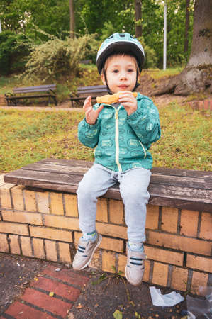 Poznan, Poland - May 17, 2020: Small two years old boy eating a waffle while sitting on a wooden park bench.Â のeditorial素材