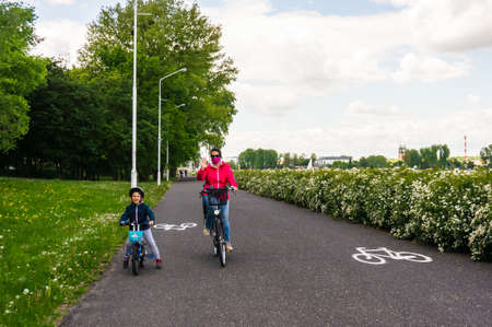 Poznan, Poland - May 17, 2020: Woman with face mask and young boy riding bicycles on a bike path in...
