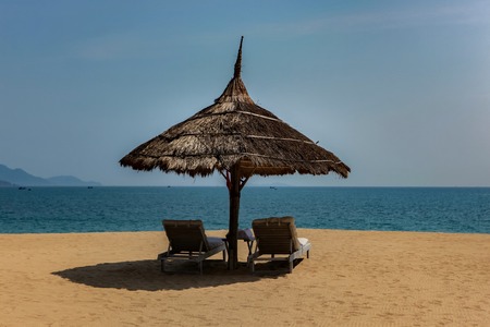 A view of Nha Trang bay in Vietnam on a sunny day with two sun lounger's under a palm umbrella.の写真素材