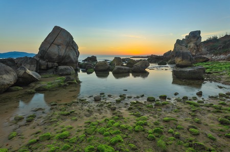 A rocky coastline sunrise with moss covered rocks looking out over the south China sea in Vung Lam Bay Vietnam.の写真素材