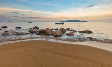 Looking out over the south china sea in Nha Trang bay just after sunset with fishing boats, large rocks and a sandy beach in the foreground.の写真素材