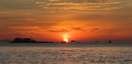 A fiery orange sunrise sky looking out over the south China sea in Nha Trang Bay Vietnam. With fishing boats in silhouette.のeditorial素材