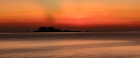 A fiery orange sunrise sky looking out over the south China sea in Nha Trang Bay Vietnam. With fishing boats and a small island in silhouette.の写真素材