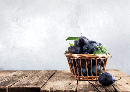 Plums on a wooden background in a wicker basketの写真素材