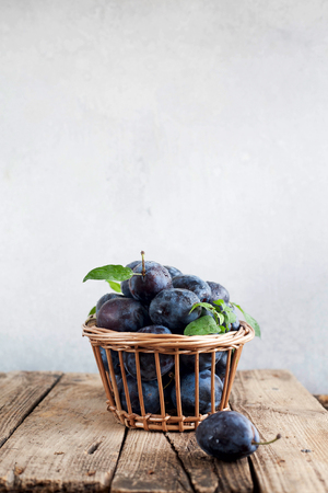 Plums on a wooden background in a wicker basketの写真素材
