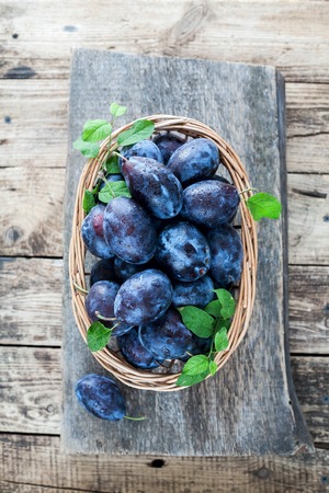 Plums on a wooden background in a wicker basketの写真素材