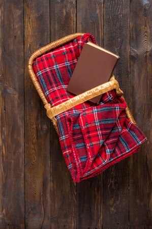 Red blanket with a book in a wicker basket on a wooden backgroundの写真素材