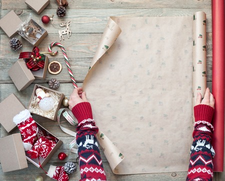 A young girl on a wooden table wraps Christmas gifts in boxes. Christmas decorations, wrapping paper, tree branches.の写真素材