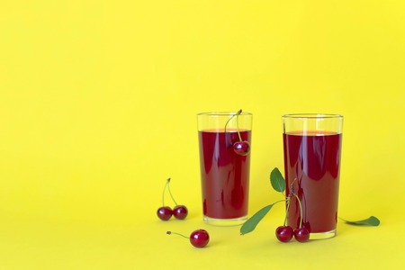 Cherry juice with cherry berries on yellow background. Copy space