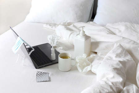 Work at home in quarantine. Laptop on the bed, tea with lemon, tablets, napkins, nasal spray, antiseptic gelのeditorial素材