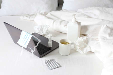 Work at home in quarantine. Laptop on the bed, tea with lemon, tablets, napkins, nasal spray, antiseptic gelのeditorial素材