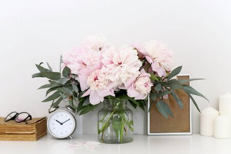 Peonies in the interior on the table, clock alarm clock, craft boxes, candlesの写真素材
