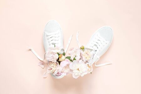 White sneakers on a pink background with peony flowers. Time of summer, time of love. Top viewの写真素材