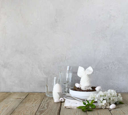 Festive table setting for Happy Easter day. On the table are plates, a fork, a knife, glasses, a...