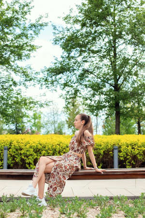 A young brunette girl in the city, in the park, sitting on a bench, drinking coffee and working on a tablet, shopping after lunch.の写真素材