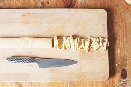 The process of cooking homemade noodles, spaghetti, pasta. On a wooden table, there is dough, a rolling pin, eggs, a board and a knife. Top view. The girl prepares homemade noodles, rolls out the dough and slices it thinly.の写真素材