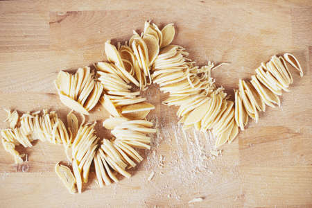 The process of cooking homemade noodles, spaghetti, pasta. On a wooden table, there is dough, a rolling pin, eggs, a board and a knife. Top view. The girl prepares homemade noodles, rolls out the dough and slices it thinly.の写真素材
