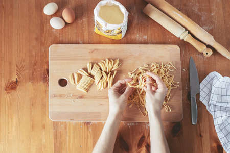 The process of cooking homemade noodles, spaghetti, pasta. On a wooden table, there is dough, a rolling pin, eggs, a board and a knife. Top view. The girl prepares homemade noodles, rolls out the dough and slices it thinly.の写真素材