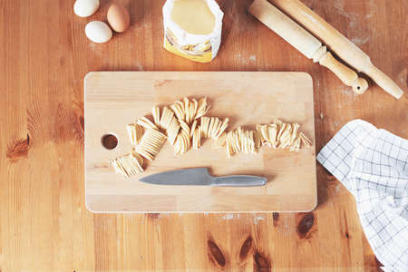 The process of cooking homemade noodles, spaghetti, pasta. On a wooden table, there is dough, a rolling pin, eggs, a board and a knife. Top view. The girl prepares homemade noodles, rolls out the dough and slices it thinly.の写真素材
