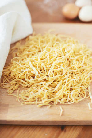 The process of cooking homemade noodles, spaghetti, pasta. On a wooden table, there is dough, a rolling pin, eggs, a board and a knife. Top view. The girl prepares homemade noodles, rolls out the dough and slices it thinly.の写真素材