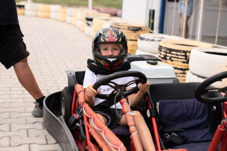A boy is sitting in a go-kart with a helmet on. Car rental for go-karting