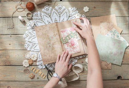Scrapbooking. On a wooden background, a girl makes a photo album for a family in a vintage style. Top viewの写真素材