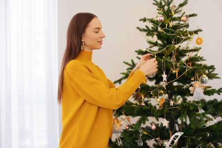 A young girl decorating a Christmas tree is sitting near the Christmas tree with a gift in her hands. Orange color in clothes. Christmas decorations.の写真素材